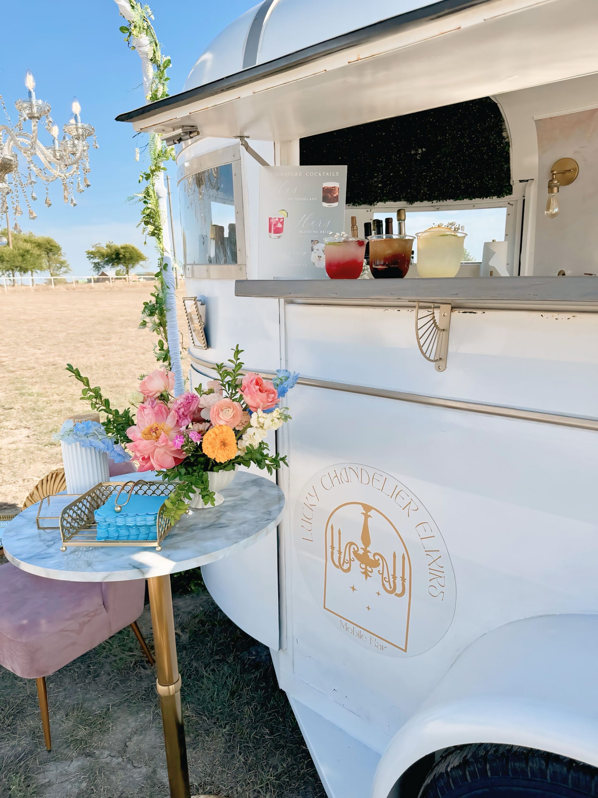 The Lucky Chandelier mobile bar trailer with signature cocktails on the counter, styled with fresh florals beneath the chandelier