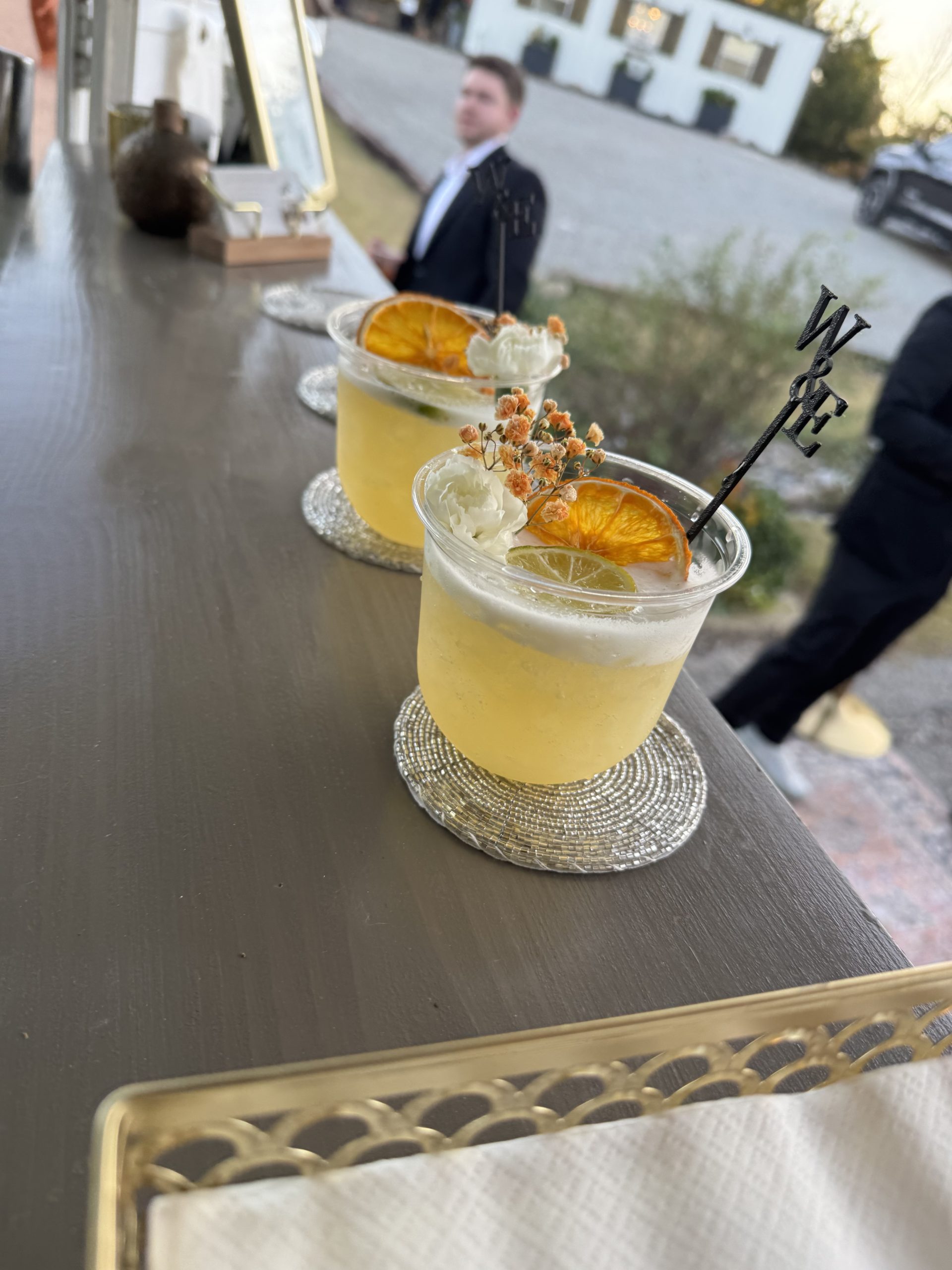 Garnished signature cocktails on the bar counter as guests gather in the background