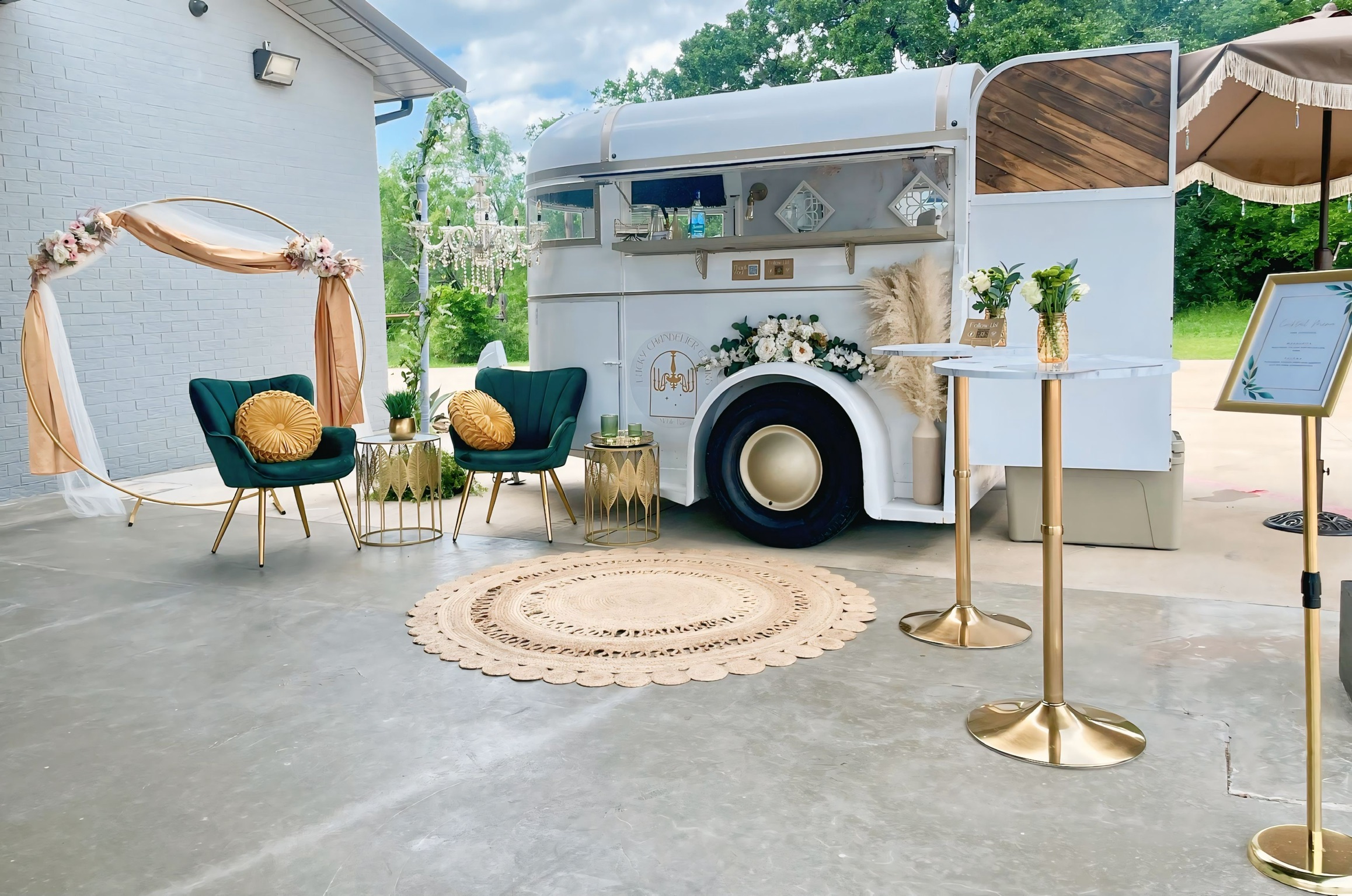 The styled Lucky Chandelier trailer and lounge setup, with a floral arch, velvet chairs, and mini chandelier post