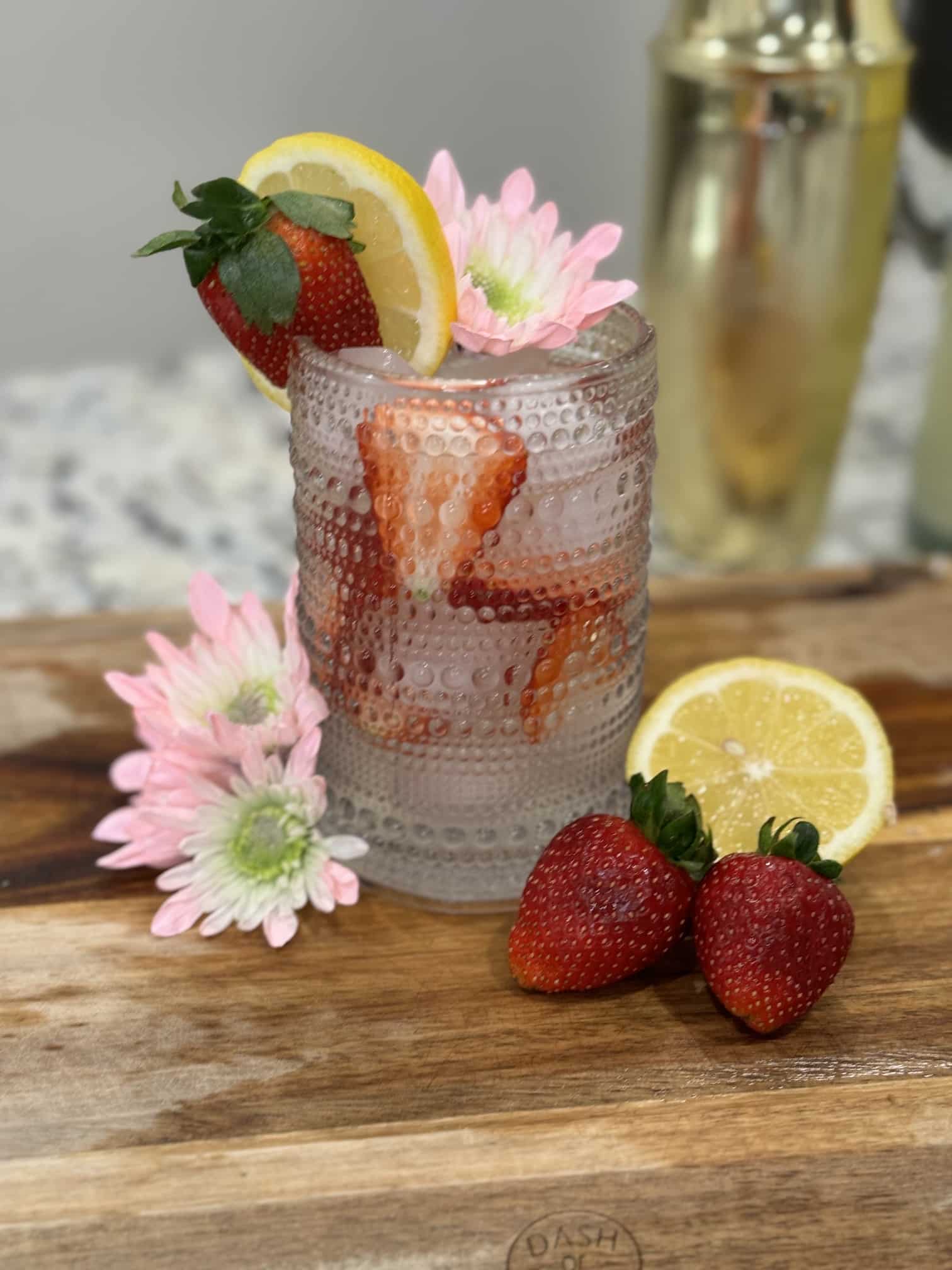 A strawberry cocktail garnished with fresh florals, served with lemon and strawberries