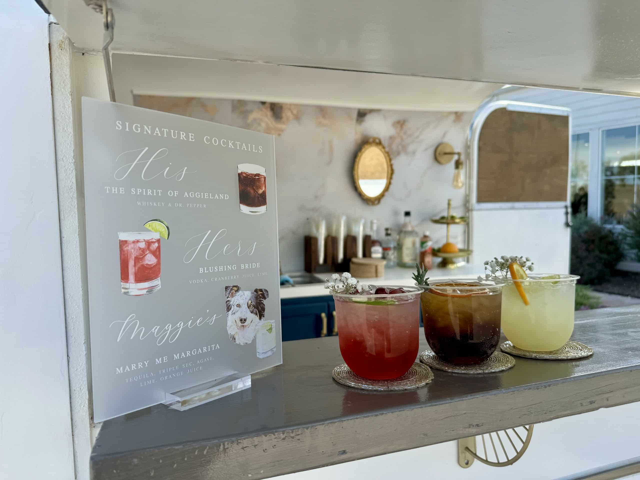 Three signature cocktails on the mobile bar counter beside a couple's personalized cocktail menu sign