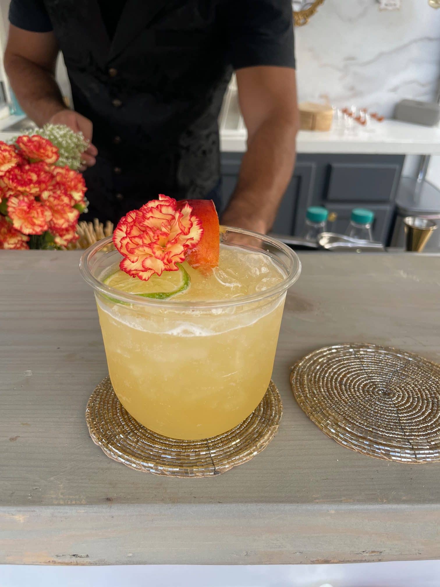 A garnished orange cocktail with a fresh carnation and peach slice